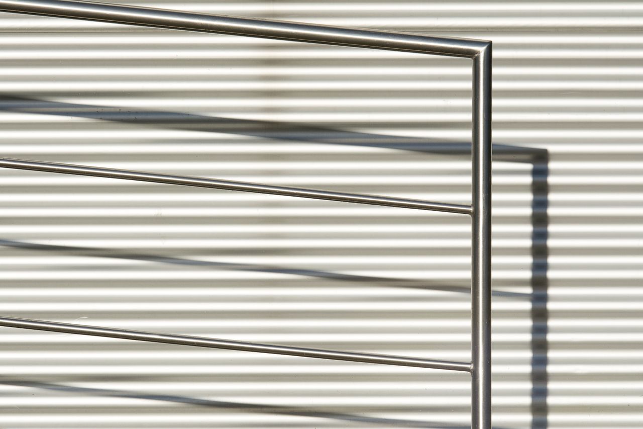 Home Close-up of a modern stainless steel railing against a striped wall background.