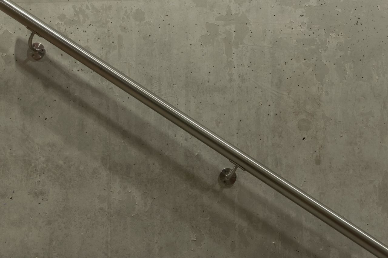Services A minimalist image of a stainless steel handrail mounted on a concrete wall.